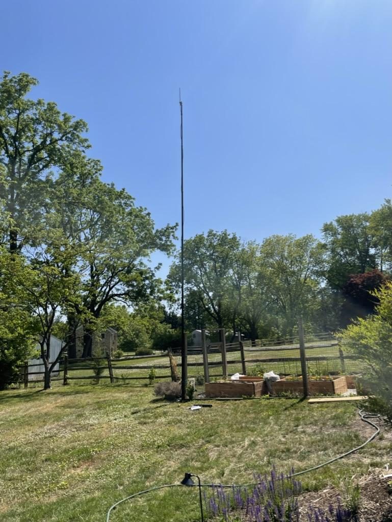 Tall fiberglass antenna pole erected in a backyard garden serving as the test base station